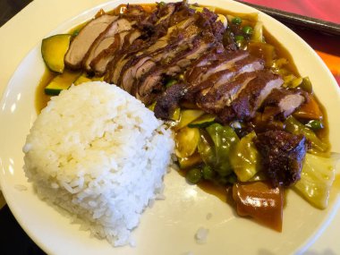 Roasted duck with rice and vegetables on white plate.