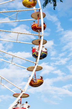 Villach, Avusturya - 29 Temmuz 2025: Açık mavi gökyüzüne karşı renkli gondolları olan parlak dönme dolap yaz şenlikleri için neşeli bir ortam yaratıyor