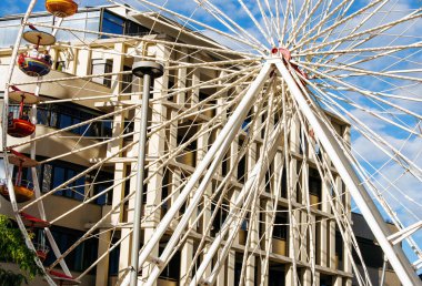 Villach, Avusturya - 29 Temmuz 2025: Renkli kulübelere sahip dönme dolap, fotokopi uzayı ile coşkulu bir ortam yaratarak çağdaş binalara karşı kurulmuştur.