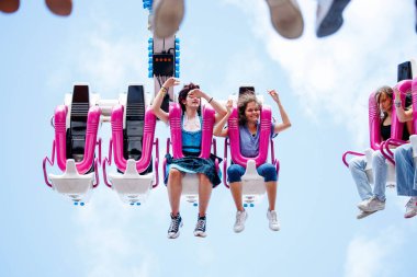 Villach, Avusturya - 29 Temmuz 2025: Genç kadınlar pembe koltuklu lunapark gezintisinden, heyecan ve yaz eğlencesini havada göstermekten heyecan duyuyorlar