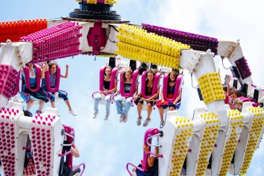 Villach, Avusturya - 29 Temmuz 2025: Heyecanlı genç kadınlar canlı renkler ve şenlikli atmosferle çevrili heyecan verici bir lunapark gezisinin tadını çıkarıyorlar