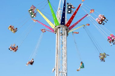Villach, Avusturya - 29 Temmuz 2025: Renkli salıncak, canlı renkler ve açık gökyüzü ile bir yaz fuarının şenlikli ruhunu somutlaştıran, yüksekten süzülen mutlu sürücüler içeriyor
