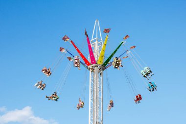 Villach, Avusturya - 29 Temmuz 2025: Renkli salıncak gezisi, açık mavi gökyüzü ile neşeli bir etkinlikte heyecan yaşayan mutlu sürücüleri içeriyor