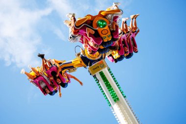 Villach, Avusturya - 29 Temmuz 2025: Festivalde heyecanlı bir lunapark gezisi, canlı koltuklarda neşeli sürücülerin yer aldığı, açık mavi gökyüzüne karşı fotokopi alanı ile kurulmuş