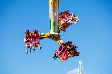 Villach, Avusturya - 29 Temmuz 2025: Heyecanlı sürücüler, renkli koltukları ve yukarıdaki parlak mavi gökyüzü ile festivalde heyecan verici bir lunapark gezisinin keyfini çıkarıyorlar