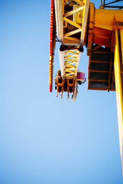 Villach, Avusturya - 29 Temmuz 2025: Heyecanlı roller coaster yolculuğu açık mavi gökyüzüne doğru süzülen parlak sarı bir yapıya sahip, eğlence parkı deneyiminin heyecanını ve neşesini gözler önüne seriyor