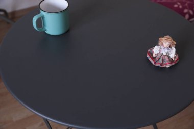 Teal kupası ve oyuncak bebek heykeli yuvarlak siyah masada.