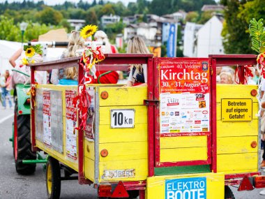 Velden, Avusturya - 30 Ağustos 2025: Ayçiçekleri ve reklamlarla süslenmiş renkli vagon, Eski Zaman Festivali 'nin şenlikli atmosferinde hareketli bir caddede ilerliyor.