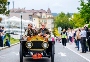 Velden, Avusturya - 30 Ağustos 2025: Antika araba severler, coşkulu izleyiciler ve hareketli sokak manzaralarıyla çevrili Oldtimer Festivali 'nde klasik bir otomobil sürüyorlar
