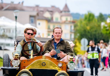 Velden, Avusturya - 30 Ağustos 2025: Antika araba severler, coşkulu kalabalık ve büyüleyici mimariyle çevrili Oldtimer Festivali 'nde klasik araba sürmenin keyfini çıkarıyorlar
