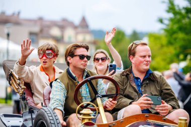 Velden, Avusturya - 30 Ağustos 2025: Genç yetişkinler klasik araçlar ve yeşilliklerle çevrili bir Oldtimer Festivali sırasında klasik bir arabada eğleniyorlar