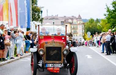 Velden, Avusturya - 30 Ağustos 2025: Klasik araba meraklıları heyecanlı seyircilerle dolu kalabalık bir sokak festivalinde klasik bir otomobili sürüyorlar