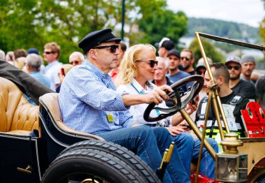 Velden, Avusturya - 30 Ağustos 2025: Eski araba severler, coşkulu bir kalabalık ve güzel bir manzarayla çevrili Oldtimer Festivali 'nde klasik bir otomobil yolculuğunun tadını çıkarıyorlar
