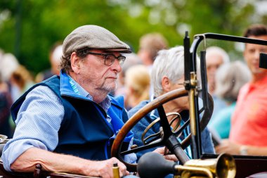 Velden, Avusturya - 30 Ağustos 2025: Yaşlı bir adam klasik bir arabada otururken eski bir festivalin atmosferinin tadını çıkarıyor