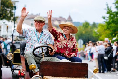 Velden, Avusturya - 30 Ağustos 2025: Eski Zaman Festivali 'nde klasik arabalar ve coşkulu kalabalıklar tarafından çevrelenmiş yaşlı çift dalgaları