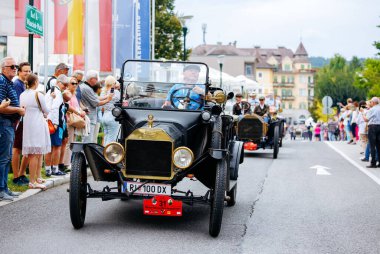 Velden, Avusturya - 30 Ağustos 2025: Antika siyah araba, klasik otomotiv tasarımı ve canlı atmosferi vurgulayarak Oldtimer Festivali 'nde coşkulu kalabalığın önünden geçiyor