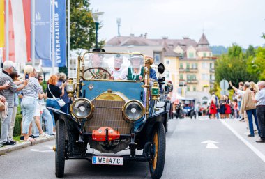 Velden, Avusturya - 30 Ağustos 2025: Klasik araba meraklıları, eski geçit töreninin keyfini çıkaran izleyicilerle dolu canlı bir festival caddesinde klasik otomobil kullanıyor