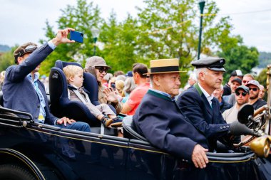 Velden, Avusturya - 30 Ağustos 2025: Klasik giyimli yaşlı erkekler, sürüşün keyfini çıkaran bir çocuk ve Oldtimer Festivali 'nde coşkulu bir kalabalık