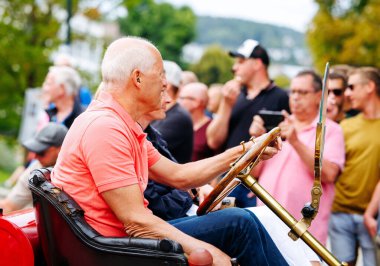Velden, Avusturya - 30 Ağustos 2025: Yaşlı adam Oldtimer Festivali 'nde klasik otomobil sürmekten hoşlanıyor, arkada heyecanlı bir kalabalık tezahürat yapıyor