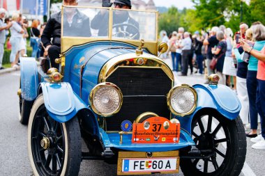 Velden, Avusturya - 30 Ağustos 2025: Oldtimer Festivali 'nden kalma klasik mavi araba kalabalığın içinden geçiyor, canlı ortamlarda klasik tasarım ve işçiliği vurguluyor