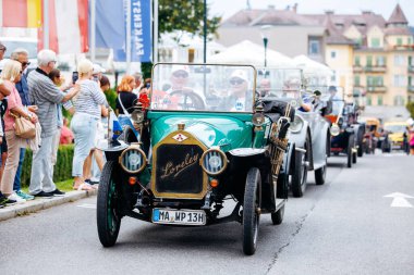 Velden, Avusturya - 30 Ağustos 2025: Eski Zaman Festivali 'nde renkli araçlar ve neşeli atmosferin keyfini çıkaran heyecanlı kalabalıkla klasik klasik araba geçidi