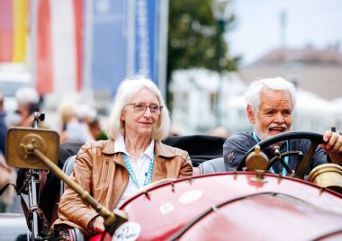 Velden, Avusturya - 30 Ağustos 2025: Yaşlı erkek ve kadın klasik araçlar ve neşeli kalabalıkla çevrili bir Oldtimer Festivali 'nde mutlu bir şekilde klasik bir araba kullanıyorlar