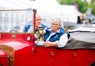 Velden, Avusturya - 30 Ağustos 2025: Vintage kırmızı araba festivalin atmosferinin tadını çıkaran ve klasik otomotiv tarihini kutlayan yaşlı bir çifti içeriden gösteriyor