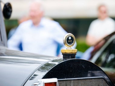 Velden, Avusturya - 30 Ağustos 2025: Klasik otomotiv etkinliğinin keyfini çıkaran bulanık izleyicilerle çevrili eski araba kaput süslemesi Oldtimer Festivali 'nde parlıyor