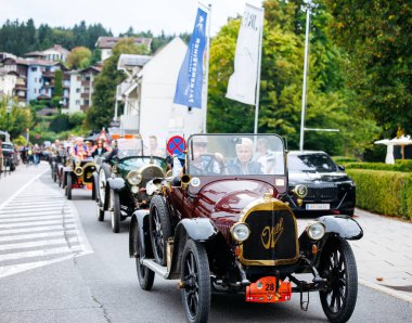 Velden, Avusturya - 30 Ağustos 2025: Klasik klasik arabalar ağaçlar ve tarihi mimariyle çevrili pitoresk bir cadde boyunca Eski Zaman Festivali 'nde geçit töreni yapıyorlar