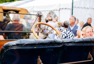 Velden, Avusturya - 30 Ağustos 2025: Klasik araba kültürünü vurgulayan festival katılımcılarıyla birlikte klasik otomobil direksiyonu odak noktasında