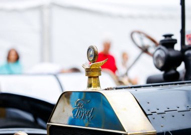 Velden, Avusturya - 30 Ağustos 2025: Klasik Ford kaput süsü, klasik arabalar ve etkinlikten keyif alan hevesli izleyicilerle çevrili Oldtimer Festivali 'nde parlıyor