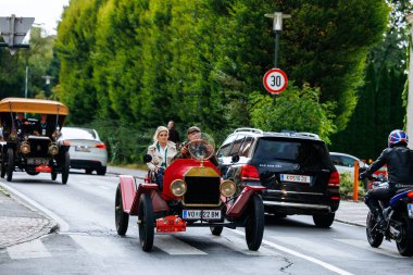 Velden, Avusturya - 30 Ağustos 2025: Antika kırmızı araba, arka planda klasik ve modern araçlarla bir Oldtimer Festivali 'nde yolda ilerliyor