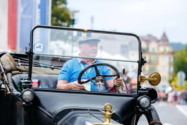 Velden, Avusturya - 30 Ağustos 2025: Yaşlı beyefendi, coşkulu izleyiciler ve canlı atmosferle çevrili, Oldtimer Festivali 'nde klasik bir arabayı sürüyor