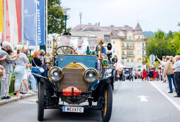 Velden, Avusturya - 30 Ağustos 2025: Klasik araba meraklıları, eski geçit töreninin keyfini çıkaran izleyicilerle dolu canlı bir festival caddesinde klasik otomobil kullanıyor