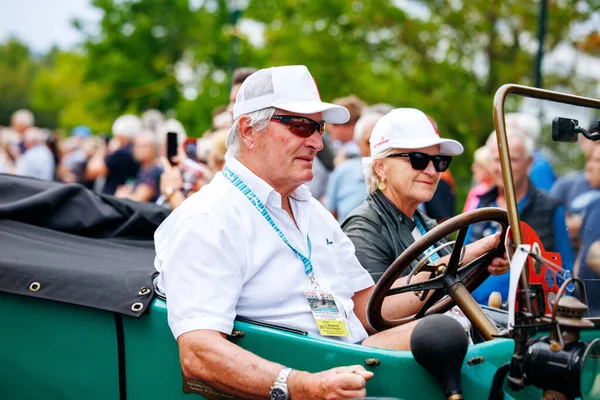 Velden, Avusturya - 30 Ağustos 2025: Yaşlı erkek ve kadın, arka planda canlı kalabalık ve yemyeşil ağaçlarla birlikte bir Oldtimer Festivali 'nde klasik bir arabada oturuyorlar