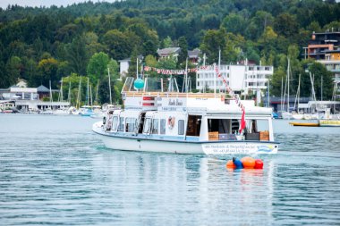 Velden, Avusturya - 30 Ağustos 2025: Sahne teknesi arka planda canlı şamandıralar ve resimli binalarla sakin göl sularında süzülüyor