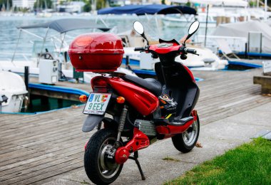 Velden, Avusturya - 30 Ağustos 2025: Kırmızı scooter marinada park halinde, tekne ve su zeminine karşı şık tasarımı ve canlı rengini vurguluyor