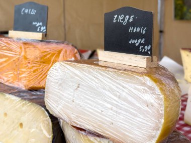 Villach, Avusturya - 12 Ocak 2026: Sanatsal peynirler, fiyatları ve türleri belirten karatahta etiketleriyle plastiğe sarılı bir pazar yerinde güzelce düzenlenmiştir.