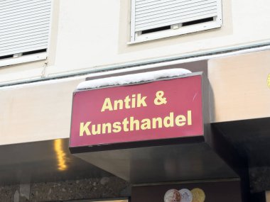 Villach, Avusturya - 12 Ocak 2026: Antika dükkanı Antik & Kunsthandel 'in bir kış mevsiminde eski eşya deposunu ön plana çıkaran güneşlik üzerindeki karla imzası