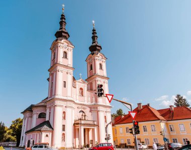 Villach, Avusturya - 14 Ağustos 2025: Ön planda ikiz kuleler ve trafik ışıklarının yer aldığı tarihi kilise, görünür renkli binalar ve açık mavi gökyüzü manzarayı güzelleştiriyor