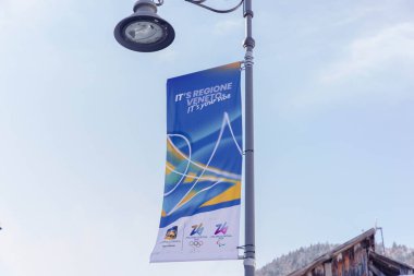 Cortina, İtalya - 27 Ocak 2026: Olimpiyat Oyunları afişi Cortina 'da bir sokak lambasına asıldı, etkinlik için canlı renkler ve bölgesel markalar sergilendi