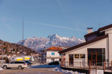 Cortina, İtalya - 27 Ocak 2026: Karlı Dolomites dağları çağdaş binaların ve park halindeki arabaların arkasında yükseliyor