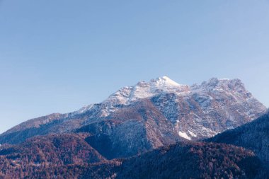 Dolomitlerin karla kaplı zirveleri, açık mavi gökyüzüne karşı parlak güneş ışığıyla aydınlatılan yemyeşil vadilerin üzerinde kuledir.
