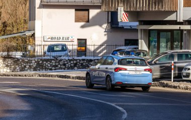 Cortina, İtalya - 27 Ocak 2026: Polis aracı 'Polizia' metniyle bir barın yakınındaki kavisli bir yolda ve dağlık bir bölgede park edilmiş çok sayıda araçta geziniyor