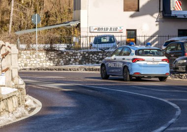 Cortina, İtalya - 27 Ocak 2026: 'Polizia' etiketli polis aracı Dolomiteler 'de kavisli bir yolda yol alırken, yakınlarda bir bar ve diğer arabalar görülebilir durumda.