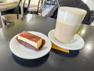 Tiramisu dilimi, sıcak latte ile sıcak kafe ortamında siyah masa üzerinde.