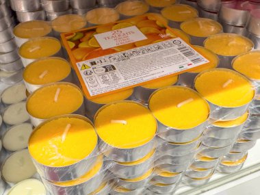 Ponte Nelle Alpi, İtalya - 27 Ocak 2026: Plastik bir kaptaki sarı çay ışığı mumları, arka planda birden fazla mum rengi sergilenen bir rafta sergilenmektedir