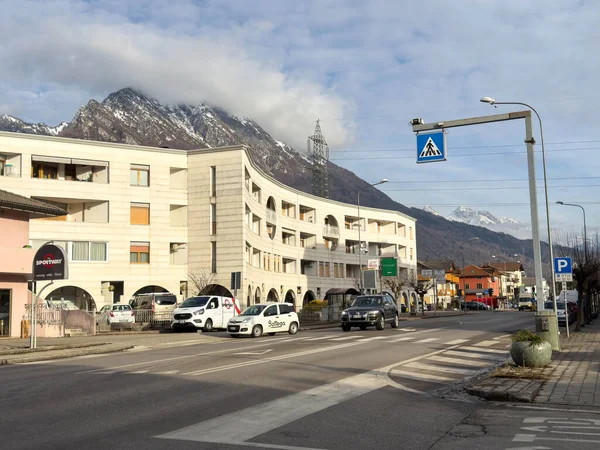 Ponte Nelle Alpi, İtalya - 27 Ocak 2026: Modern mimari, park edilmiş araçlar ve arka planda yaya geçidi tabelasıyla birlikte dağların yer aldığı şehir sokak sahnesi
