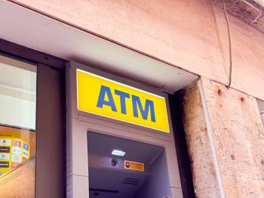 Venedik, İtalya - 17 Şubat 2026: Cam yansımalı kentsel alanda dokulu taş bir duvara sarı tabelalı ATM makinesi