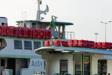 Venedik, İtalya - 7 Şubat 2026: Üst güvertede kırmızı can yelekleri ve ön teknede yeşil bir bayrak bulunan iki feribot bir limana demirlemiştir.
